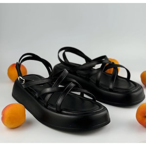 May include: Two pairs of black leather platform sandals with criss-cross straps. The sandals have a chunky platform sole and an ankle strap.