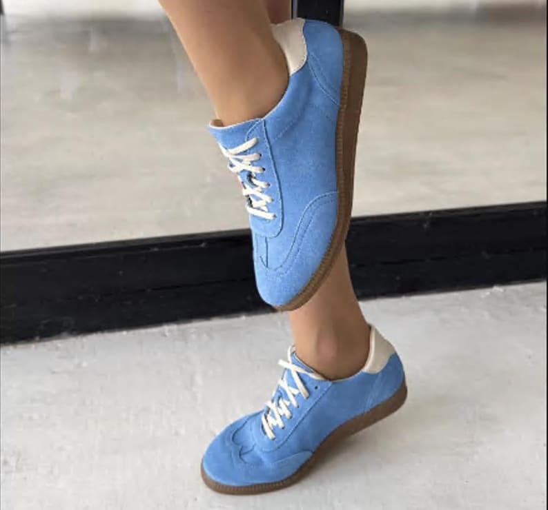 May include: A pair of light blue suede trainers with white laces and a white trim around the ankle. The trainers have a brown rubber sole.