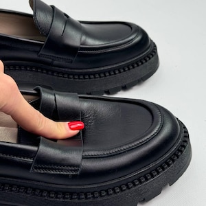 Puede incluir: Zapatos de vestir negros de cuero con suela de plataforma gruesa. Los zapatos de vestir tienen un dise&ntilde;o sencillo con una sola correa en la parte superior.