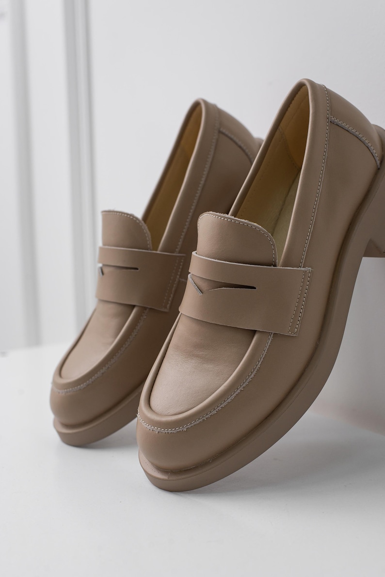 K&ouml;nnte beinhalten: Ein Paar hellbraune Lederschuhe mit einem schlichten Design. Die Schuhe haben eine abgerundete Spitze und eine Naht um den Rand der Sohle.