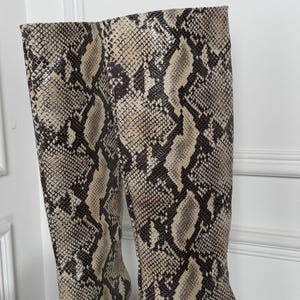 May include: A pair of knee-high boots with a snakeskin pattern in shades of brown, tan, and black. The boots have pointed toes and stiletto heels. The boots are made of a textured material.