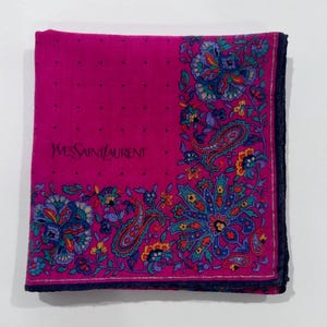 Puede incluir: Un pa&ntilde;uelo de seda rosa con un patr&oacute;n de paisley y el texto "Yves Saint Laurent" en negro.
