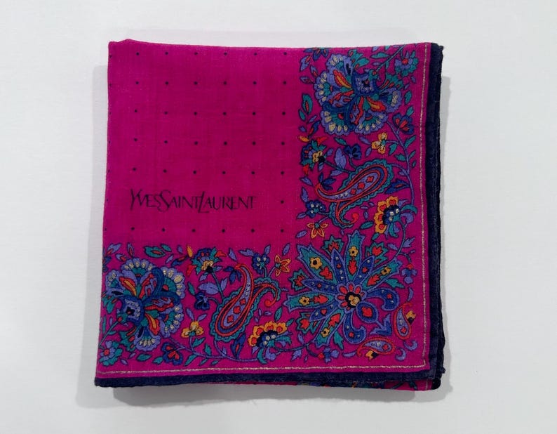Puede incluir: Un pa&ntilde;uelo de seda rosa con un patr&oacute;n de paisley y el texto "Yves Saint Laurent" en negro.