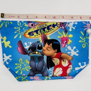 May include: Blue drawstring pouch featuring a graphic of Stitch and Lilo from the animated film. The pouch has a blue background with yellow and white splatters. The text "626 Experiment" is printed on the pouch. The pouch is approximately 10 inches wide.