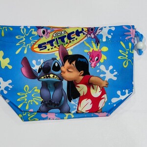 May include: A blue drawstring bag featuring Stitch and Lilo from the animated film Lilo & Stitch. The bag has a blue background with white splatters and the words "626 Experiment Stitch". The bag is approximately 8 inches wide.
