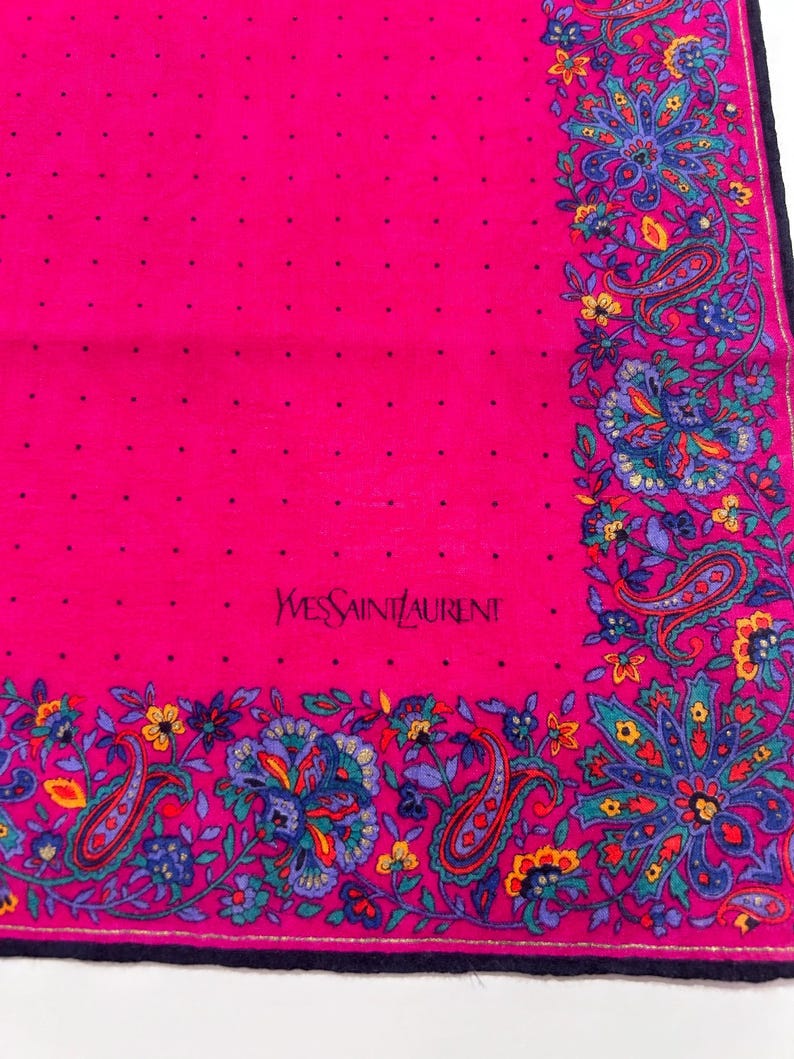 Puede incluir: Un pa&ntilde;uelo de seda rosa con un patr&oacute;n de lunares blancos y un borde paisley. El pa&ntilde;uelo tiene el texto "Yves Saint Laurent" bordado en negro.