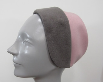 May include: A two-tone headband in gray and pink. The headband is made of a soft material and is displayed on a mannequin head. The gray band covers the forehead, while the pink covers the top of the head.