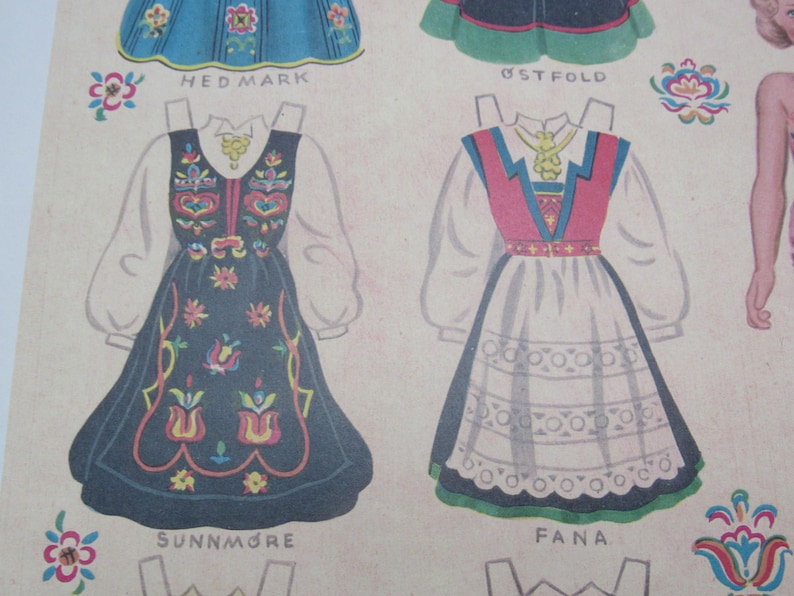 Puede incluir: Mu&ntilde;ecas de papel vintage con vestidos folcl&oacute;ricos noruegos tradicionales. Los vestidos est&aacute;n intrincadamente dise&ntilde;ados con patrones florales y bordados, en colores como el azul, el rojo y el blanco. Los nombres "HEDMARK", "SUNNM&Oslash;RE" y "FANA" est&aacute;n impresos debajo.