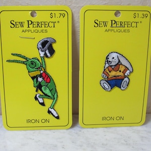 May include: Two Sew Perfect iron-on appliques on yellow backing cards. The left card features a green grasshopper wearing a top hat, red tie, and black shoes. The right card features a white rabbit wearing an orange shirt and blue pants.