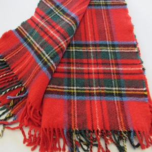 May include: A red and green plaid scarf with fringed edges. The scarf features a classic tartan pattern with red as the primary color, accented by green, blue, black, and white stripes. The fringed edges add a decorative touch.