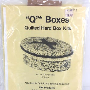 May include: A package for a quilted hard box kit. The kit includes an oval box with a floral pattern and a black cross design on the lid. The box is 3.75" x 6" inside and 2" deep. The text on the package reads "Q Boxes".