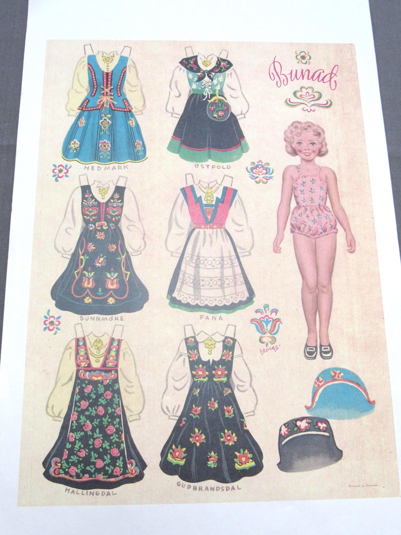 Puede incluir: Una hoja de mu&ntilde;eca de papel vintage con trajes folcl&oacute;ricos tradicionales noruegos, o bunads. La hoja incluye varios dise&ntilde;os de vestidos detallados, una mu&ntilde;eca de papel y accesorios como sombreros. Los vestidos son de varios colores con patrones florales y geom&eacute;tricos.