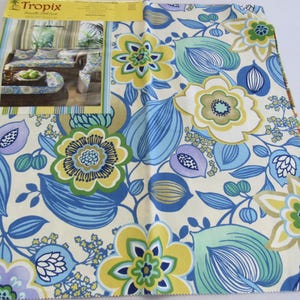 May include: A fabric swatch featuring a floral pattern in shades of blue, yellow, green, and purple on a cream background. The design includes large stylized flowers and leaves. The top of the swatch has a printed image with the text "Tropix".