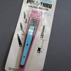 May include: A Dyno Elastic Pull-Thru lacing ribbon tool in a pink and light blue plastic design, packaged on a white card with black instructional diagrams. The packaging features the text PULL-THRU, ELASTIC, LACING RIBBON, and ITEM 314.
