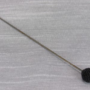 May include: A long, slender metal sewing pin featuring a round, textured black head. The pin has a sharp, pointed tip at one end and a spherical, beaded-style black head at the other, designed for securing fabric during sewing or tailoring tasks.