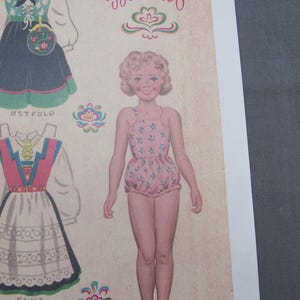 Puede incluir: Hoja de mu&ntilde;eca de papel vintage con una ni&ntilde;a en un traje de ba&ntilde;o rosa floral y varios trajes folcl&oacute;ricos noruegos tradicionales. La palabra "Bunad" est&aacute; escrita en cursiva encima de la mu&ntilde;eca. Los trajes incluyen vestidos con patrones florales y geom&eacute;tricos.