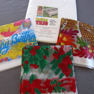 May include: A selection of plastic tablecloths and runners. One runner displays "Happy Birthday" in blue script. Other runners feature festive designs in red, green, and orange. A package of Holiday Trio tablecloths and runners is also included.