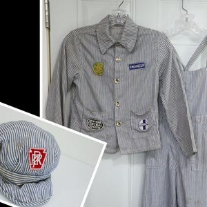 May include: A blue and white hickory striped engineer jacket and matching overalls set with various embroidered patches including one that reads ENGINEER and another NEW YORK CENTRAL SYSTEM, paired with a matching striped train conductor cap.