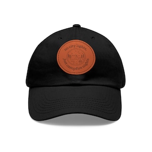 May include: Black baseball cap with a brown leather patch that says "no city lights, just campfire nights". The patch features a camping scene with a tent, campfire, and trees.