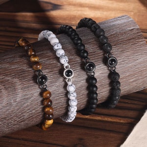 May include: Four beaded bracelets with black accents. The bracelets are made of tiger's eye, white stone, black lava rock, and black onyx beads.