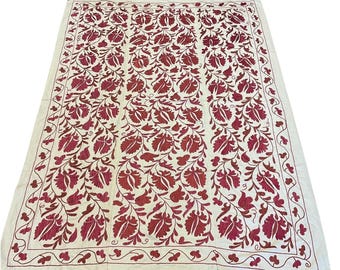 May include: A large, rectangular, off-white textile with an intricate embroidered floral pattern in shades of red. The design features stylized flowers and leaves, with a detailed border. The textile is likely a decorative item, such as a tablecloth or wall hanging.