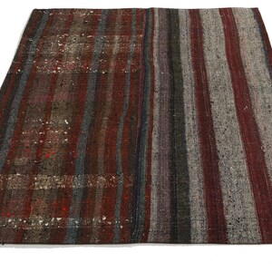 Op de afbeelding: Een vintage gestreept tapijt met een mix van rode, bruine, grijze en blauwe tinten. Het tapijt heeft een verweerde look en is gemaakt van wol.