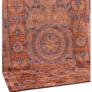 Può includere: Un tappeto rettangolare dettagliato con un colore di base marrone rossastro caldo. Il tappeto presenta motivi intricati in tonalità di blu, beige e marrone, inclusi disegni floreali e geometrici. Il design del tappeto è simmetrico, con un medaglione centrale e bordi.