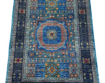 May include: A blue and green rug with a geometric pattern. The rug has a central medallion with a red, orange, and yellow design. The rug is surrounded by a border of blue and green.