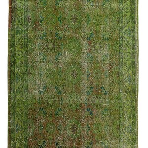 Könnte beinhalten: Ein rechteckiger, verwaschen grüner Teppich mit detailliertem Blumenmuster. Der Teppich weist Grüntöne, Braun und Blau auf und hat ein verblasstes, Vintage-Aussehen. Der Rand hat ein dunkleres grünes, verziertes Design.