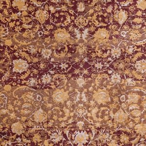 Può includere: Primo piano di un tappeto con un motivo floreale dettagliato. Il tappeto presenta una ricca tavolozza di colori bordeaux, oro e crema. Il design include intricati motivi floreali e a volute, creando un aspetto lussuoso e ornato. La trama del tappeto appare morbida e invitante.
