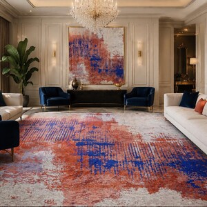 Può includere: Un lussuoso soggiorno con un grande tappeto dal design astratto nei toni del rosso, blu e bianco. La stanza comprende due divani bianchi, due poltrone blu e una grande opera d'arte astratta. L'ambiente è luminoso.