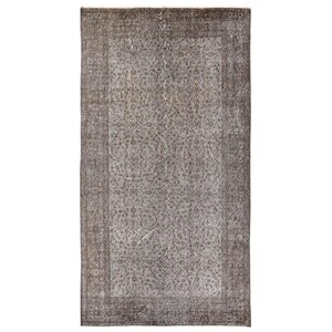 May include: A vintage rug with a faded floral pattern in shades of gray and brown. The rug has a border with a more intricate design.