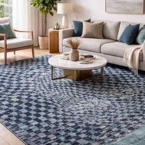 Può includere: Un tappeto a motivi blu e bianchi con un design geometrico. Il tappeto si trova in un soggiorno, con un divano, un tavolino e una poltrona visibili. Il motivo del tappeto è un design quadrato ripetuto.