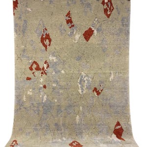 May include: A rectangular rug with a beige background and a pattern of red and blue abstract shapes. The rug has a textured appearance and a fringe along the bottom edge. The rug is hanging from metal clips.