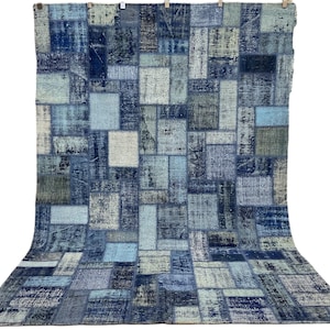 Può includere: Un tappeto patchwork blu e bianco con un motivo geometrico. Il tappeto è realizzato in denim riciclato e ha un aspetto vissuto.