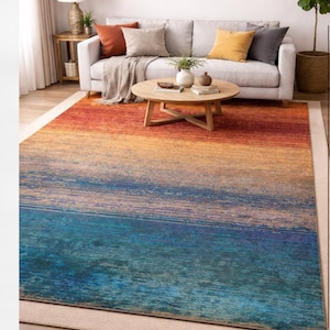 Può includere: Un tappeto rettangolare con un design sfumato, che passa dal rosso-arancio al giallo, poi al blu. Il tappeto è posizionato su un pavimento chiaro, con un divano e un tavolino sullo sfondo. Il tappeto misura circa 244 x 305 cm.