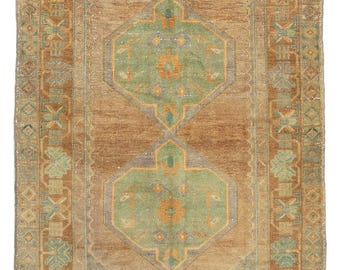 Könnte beinhalten: Ein Vintage-Teppich mit braunem Hintergrund und einem zentralen Design mit zwei Achtecken mit grünen, blauen und orangefarbenen Akzenten. Der Teppich hat einen Rand mit einem sich wiederholenden Muster aus geometrischen Formen in Braun, Blau und Grün.