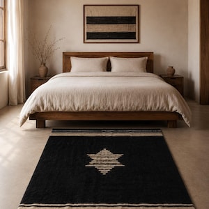 Può includere: Camera da letto con letto in legno, biancheria da letto beige e tappeto nero. Il tappeto ha un design a stella e strisce beige. Un'opera d'arte incorniciata con strisce nere e beige è appesa sopra il letto.