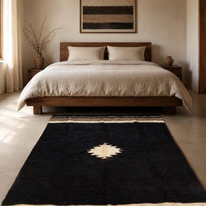 Può includere: Camera da letto con letto in legno, biancheria da letto beige e tappeto nero con motivo centrale color crema e strisce marroni. Un'opera d'arte incorniciata è appesa sopra il letto. La stanza ha una palette di colori neutri.