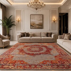 Può includere: Un grande tappeto ornato con un design a medaglione centrale nei toni del rosso, arancione e grigio. Il tappeto è posto in un lussuoso soggiorno con mobili dai toni neutri e un lampadario.