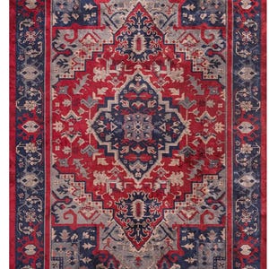 Può includere: Un tappeto rettangolare con un motivo dettagliato e simmetrico. Il tappeto presenta un campo centrale rosso con un design complesso in blu navy, grigio e crema. Un bordo blu navy incornicia il design, con un bordo esterno rosso. Il design del tappeto ricorda i tradizionali tappeti persiani.