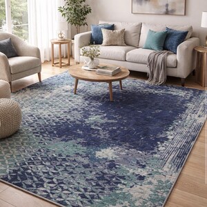 Può includere: Un grande tappeto con un motivo geometrico nei toni del blu, verde acqua e grigio. Il tappeto è collocato in un soggiorno con un divano, sedie e un tavolino. Il tappeto misura circa 244 x 305 cm.