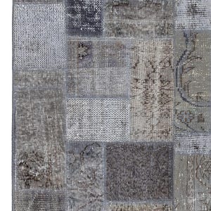 Op de afbeelding: Een patchwork tapijt met verschillende grijze en bruine tinten. Het tapijt is gemaakt van verschillende stoffen en texturen, wat een uniek en interessant ontwerp creëert.
