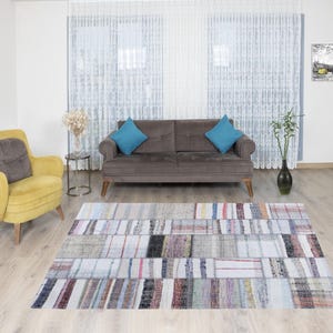 Può includere: Un tappeto patchwork bianco, grigio e multicolore con un divano marrone e una poltrona gialla sullo sfondo.