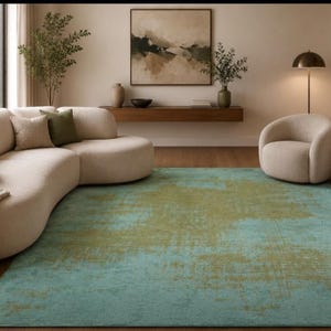 Può includere: Un moderno soggiorno con un grande divano beige curvo e diversi cuscini. Un tappeto turchese e oro copre il pavimento. Una poltrona abbinata è nelle vicinanze. Un dipinto è appeso al muro sopra una mensola di legno.