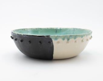 May include: A ceramic bowl with a black and white glaze and a green rim. The bowl has a textured rim with small bumps.