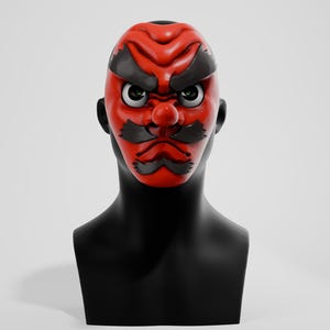 May include: A vibrant red Japanese demon mask with black detailing, including eyebrows and a mustache. The mask is mounted on a black mannequin head, set against a plain white backdrop. A striking piece of cultural art.