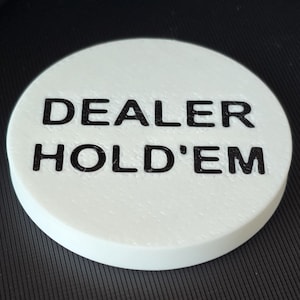 May include: White round poker chip with black text that reads "DEALER HOLD'EM".