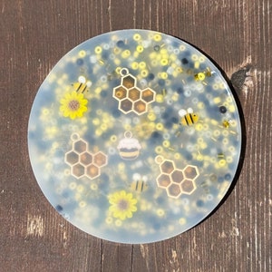 Puede incluir: Un posavasos redondo transparente con un dise&ntilde;o de abeja y panal. El posavasos est&aacute; decorado con cuentas amarillas, negras y blancas.