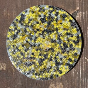 Puede incluir: Un posavasos redondo de resina transparente con un dise&ntilde;o de mosaico de cuentas negras, blancas y amarillas.